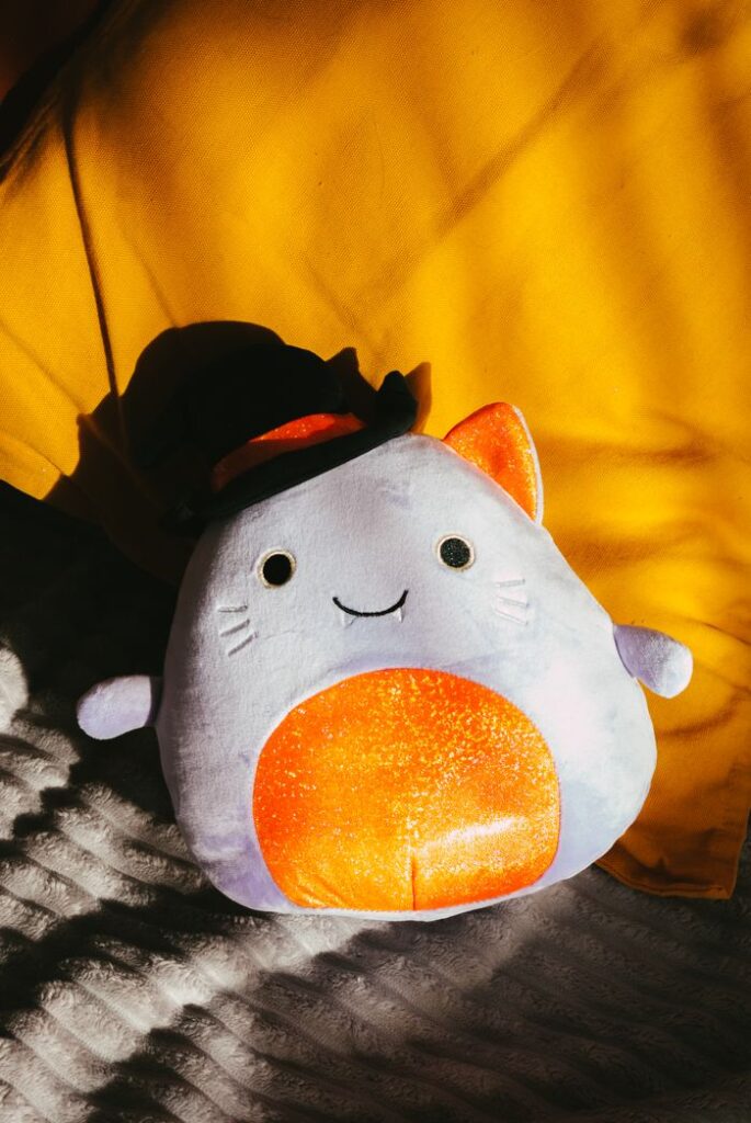 Cute plush cat toy sunlit on yellow and white bedding. Perfect for cozy or playful home decor.